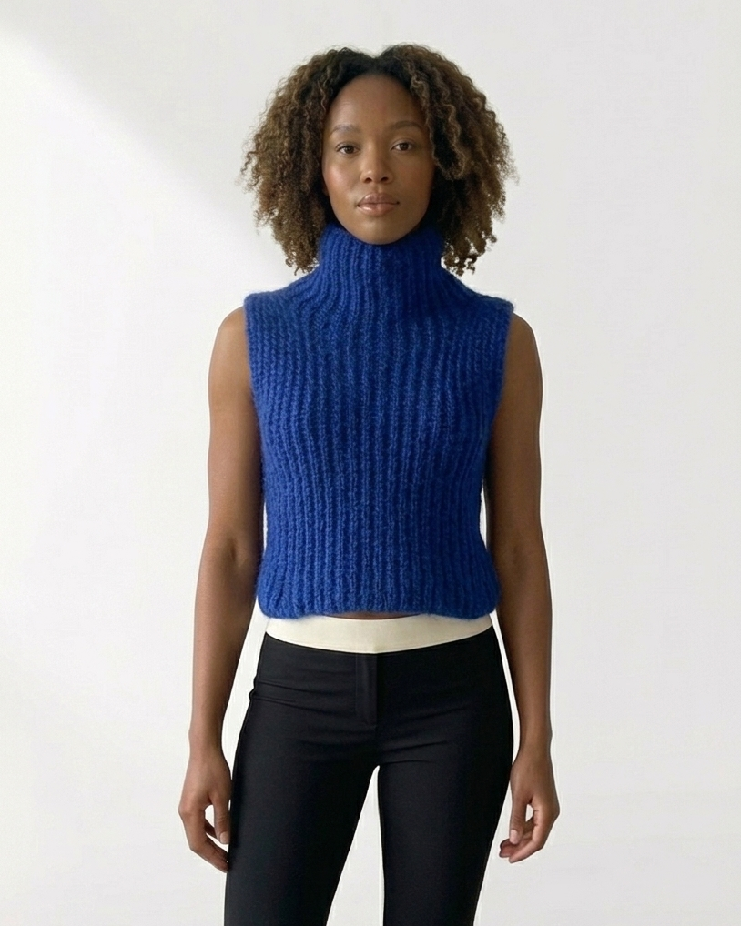 South African model wearing sleeveless cobalt blue chunky knit turtleneck vest with long beaded necklace and green tassel. High neck ribbed sweater showcases South African craftsmanship, Studio Minimale