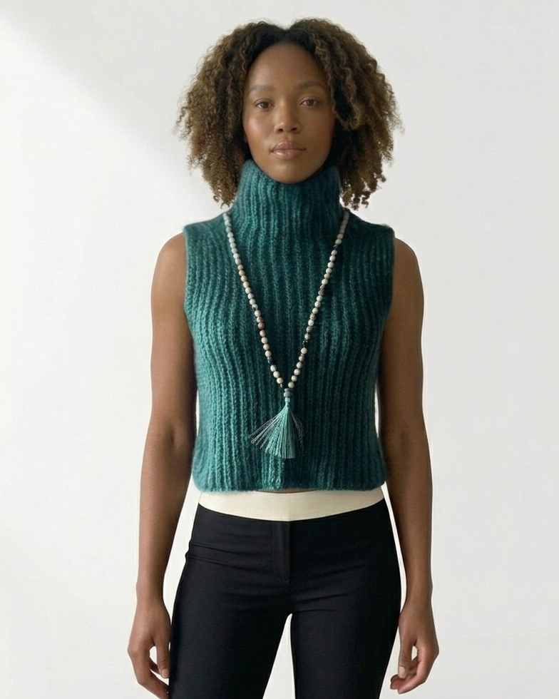 South African model wearing sleeveless green chunky knit turtleneck vest with long beaded necklace and green tassel. High neck ribbed sweater showcases South African craftsmanship, Studio Minimale