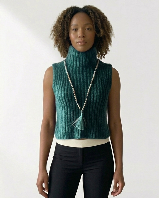 South African model wearing sleeveless green chunky knit turtleneck vest with long beaded necklace and green tassel. High neck ribbed sweater showcases South African craftsmanship, Studio Minimale